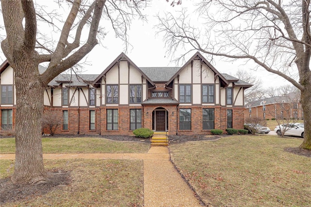 tudor house with a shingled roof, a front yard, brick siding, and stucco siding