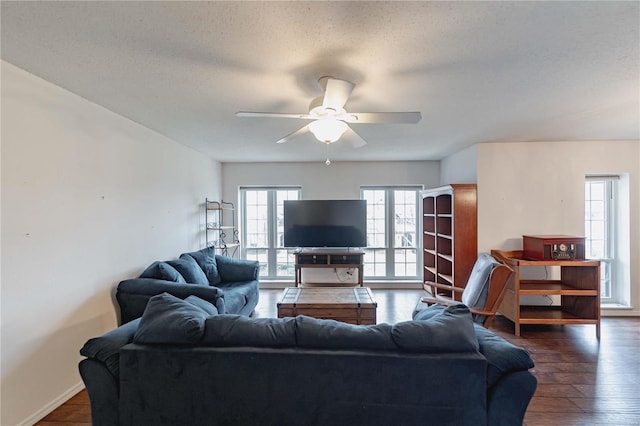 living area featuring a textured ceiling, dark wood finished floors, a ceiling fan, and baseboards