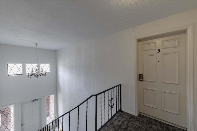 foyer featuring a chandelier, dark colored carpet, and a textured ceiling