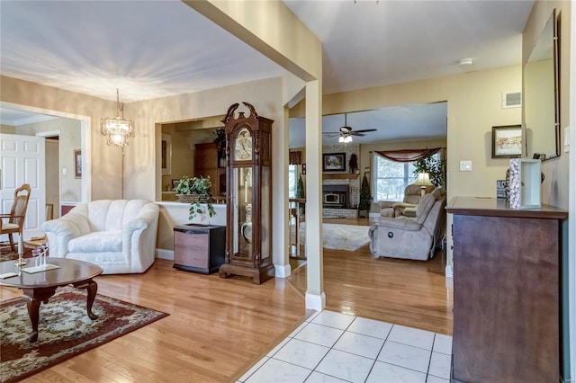 living room with ceiling fan with notable chandelier, a brick fireplace, light wood-style flooring, and visible vents