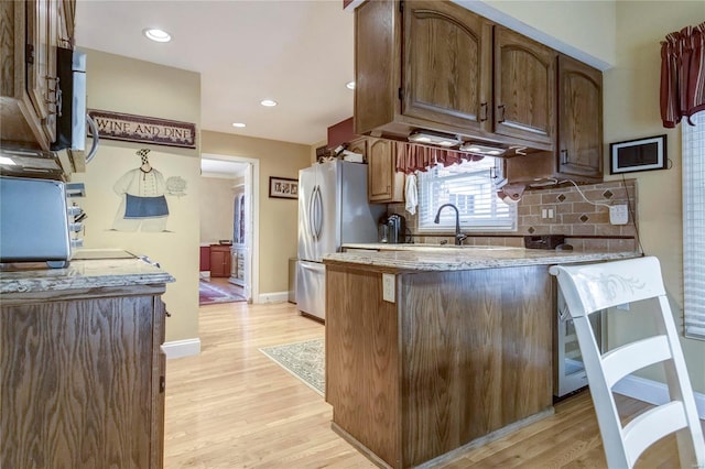 kitchen featuring a sink, tasteful backsplash, freestanding refrigerator, a peninsula, and light wood finished floors