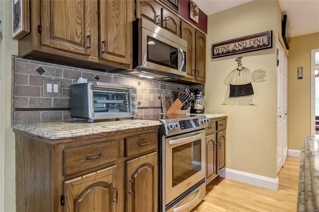 kitchen featuring light wood-style flooring, backsplash, appliances with stainless steel finishes, a toaster, and baseboards