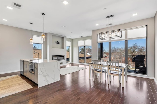 kitchen featuring light stone countertops, dark wood-type flooring, a sink, and a glass covered fireplace