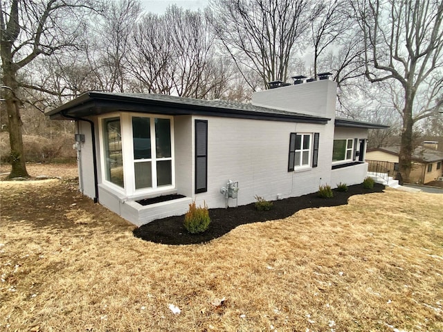 view of property exterior featuring a yard, a chimney, and brick siding