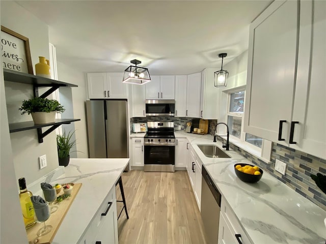 kitchen featuring light wood finished floors, tasteful backsplash, appliances with stainless steel finishes, white cabinetry, and a sink