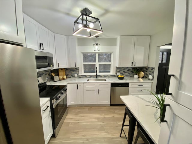 kitchen with appliances with stainless steel finishes, white cabinetry, a sink, and light wood-style flooring