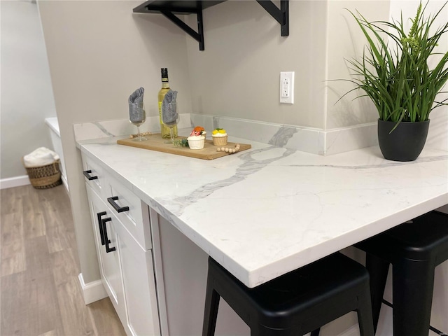 interior space with light stone counters, a peninsula, white cabinetry, a kitchen breakfast bar, and light wood finished floors