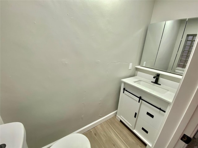 half bathroom featuring baseboards, vanity, toilet, and wood finished floors