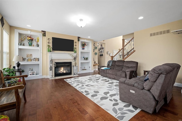 living area featuring dark wood-type flooring, a fireplace with flush hearth, visible vents, built in features, and stairway