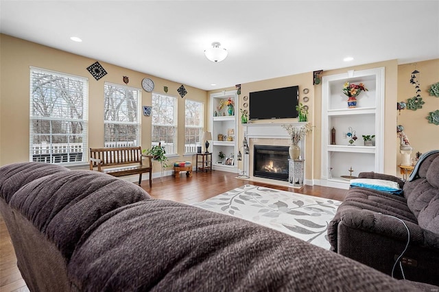 living area with built in features, plenty of natural light, a fireplace with flush hearth, and wood finished floors