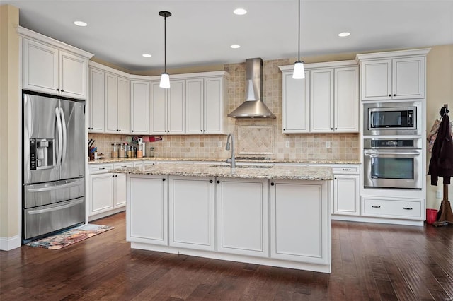 kitchen featuring light stone counters, dark wood-style floors, appliances with stainless steel finishes, a kitchen island with sink, and wall chimney exhaust hood