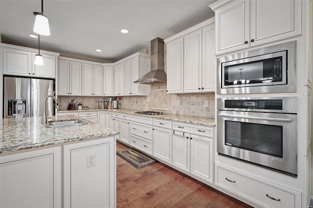 kitchen with stainless steel appliances, wood finished floors, a sink, wall chimney range hood, and decorative backsplash