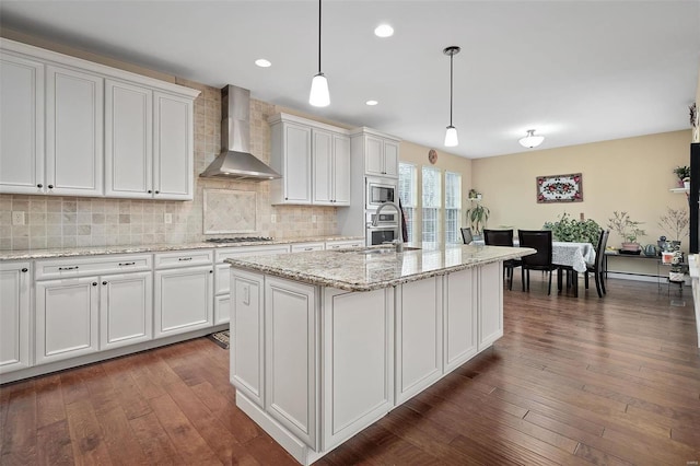 kitchen featuring decorative backsplash, white cabinets, wall chimney exhaust hood, appliances with stainless steel finishes, and dark wood-style flooring