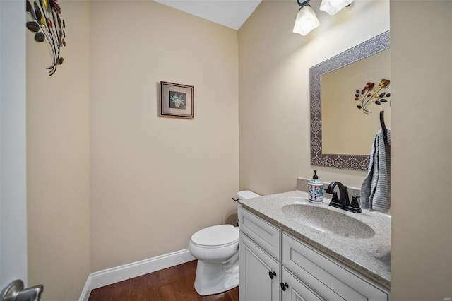 half bath with toilet, wood finished floors, vanity, and baseboards