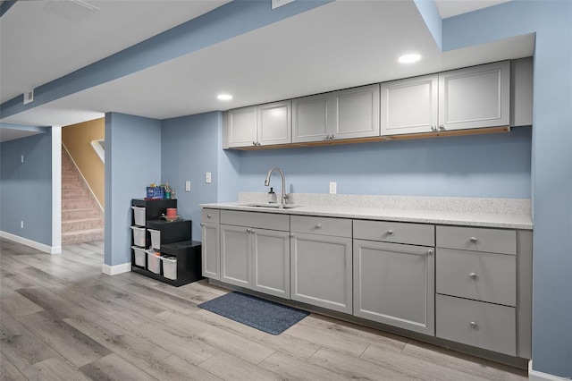 kitchen with gray cabinets, baseboards, a sink, and light wood finished floors