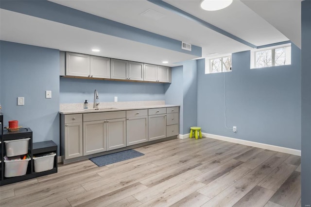 kitchen with light wood finished floors, a sink, visible vents, and gray cabinetry