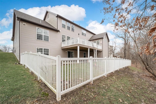 rear view of property featuring a lawn, a balcony, and fence