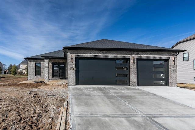 prairie-style house with a garage, concrete driveway, brick siding, and a shingled roof