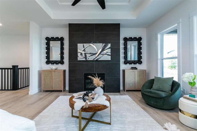 living area featuring a raised ceiling, wood finished floors, and a tile fireplace