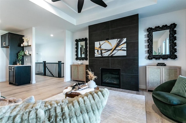 living room with baseboards, a raised ceiling, ceiling fan, light wood-type flooring, and a fireplace