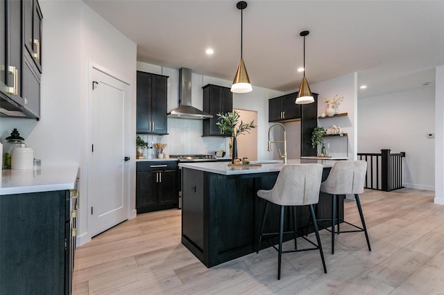 kitchen with a sink, light countertops, wall chimney range hood, dark cabinetry, and decorative backsplash