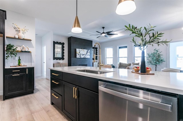 kitchen with plenty of natural light, dark cabinets, light countertops, stainless steel dishwasher, and a sink