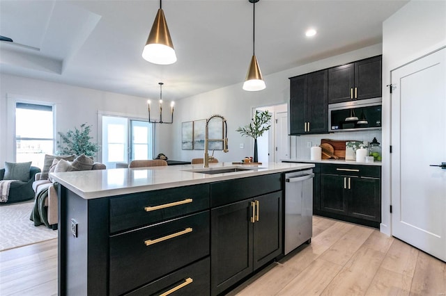 kitchen featuring stainless steel appliances, light countertops, light wood-style flooring, a sink, and dark cabinets