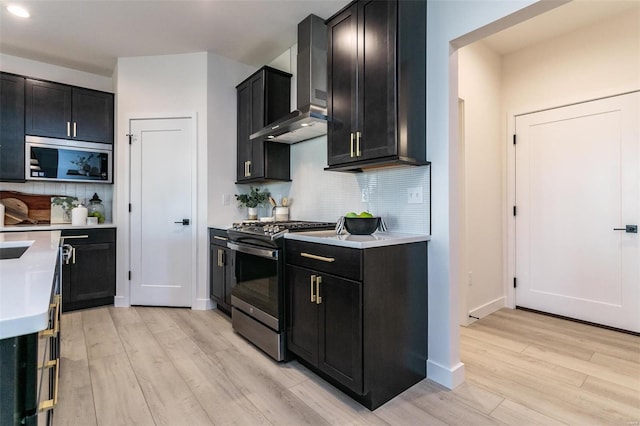 kitchen featuring wall chimney range hood, dark cabinetry, light countertops, and stainless steel range with gas stovetop