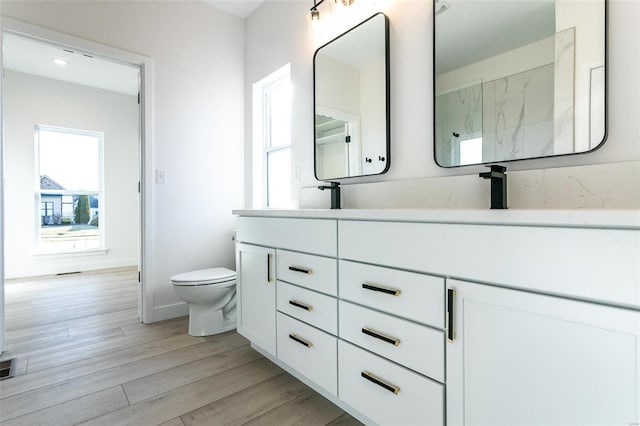 bathroom featuring double vanity, toilet, a sink, wood finished floors, and baseboards