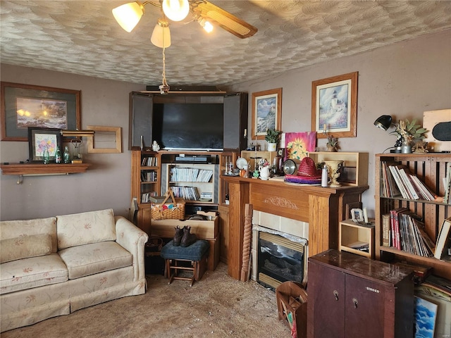 living room featuring a glass covered fireplace, ceiling fan, and a textured ceiling