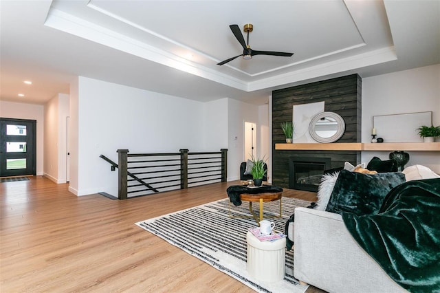 living area with baseboards, a raised ceiling, a ceiling fan, wood finished floors, and a fireplace