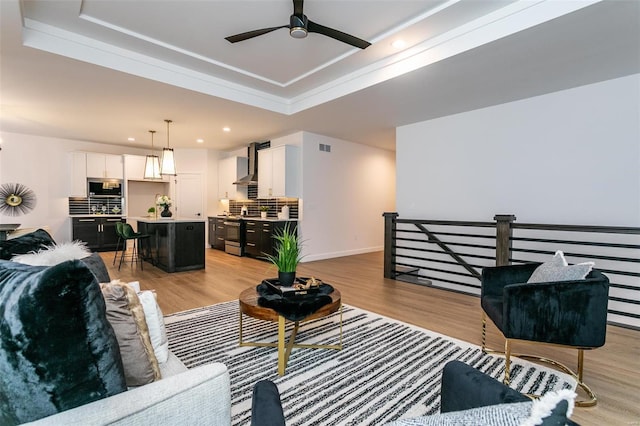 living area with visible vents, a raised ceiling, ceiling fan, light wood-type flooring, and recessed lighting