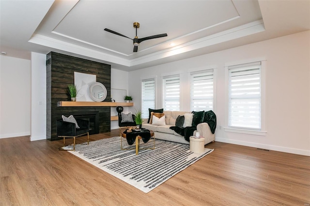 living room featuring wood finished floors, a tray ceiling, and a glass covered fireplace