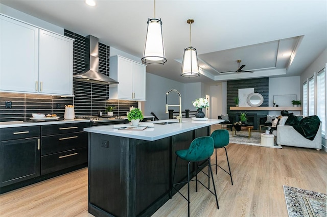 kitchen with a sink, light countertops, light wood-type flooring, wall chimney exhaust hood, and a tray ceiling