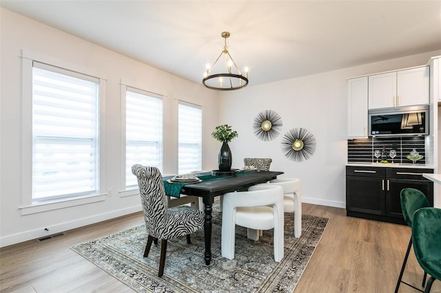 dining room with light wood-style floors, baseboards, visible vents, and a notable chandelier