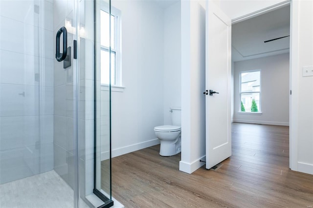 bathroom with baseboards, wood finished floors, toilet, and a shower stall