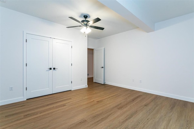 unfurnished bedroom with beam ceiling, a closet, light wood-style floors, ceiling fan, and baseboards