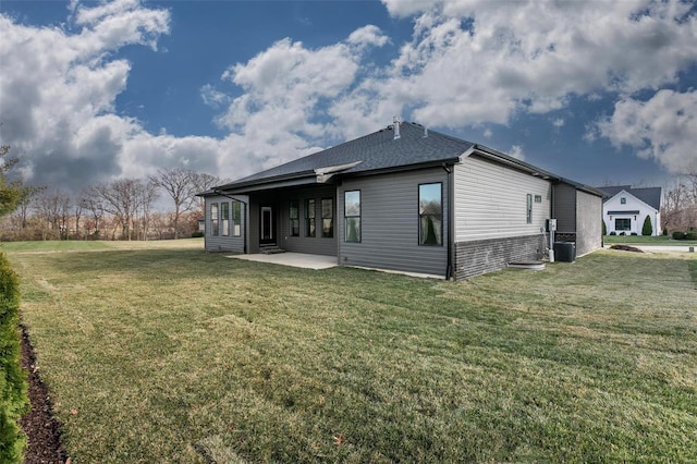 back of house with central AC unit, a lawn, a patio area, and a shingled roof