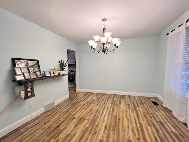 unfurnished dining area featuring baseboards, visible vents, an inviting chandelier, and wood finished floors