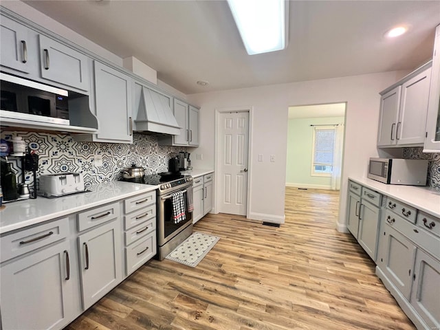 kitchen with stainless steel appliances, custom exhaust hood, and gray cabinetry