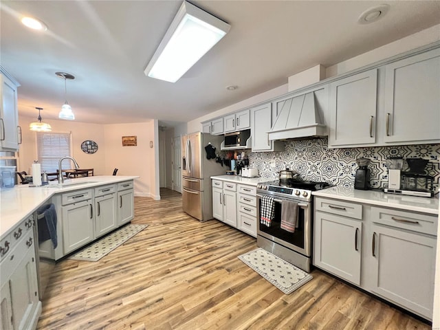 kitchen with light wood finished floors, tasteful backsplash, appliances with stainless steel finishes, a peninsula, and premium range hood