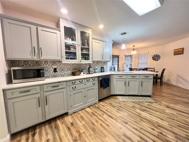 kitchen with decorative backsplash, appliances with stainless steel finishes, a peninsula, light wood-type flooring, and a sink