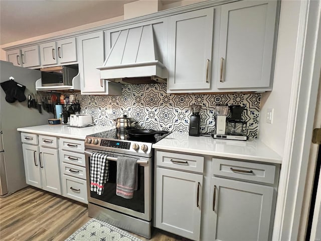 kitchen featuring stainless steel appliances, light countertops, custom exhaust hood, and tasteful backsplash