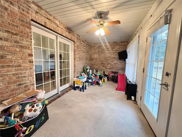 interior space featuring ceiling fan, brick wall, and carpet floors