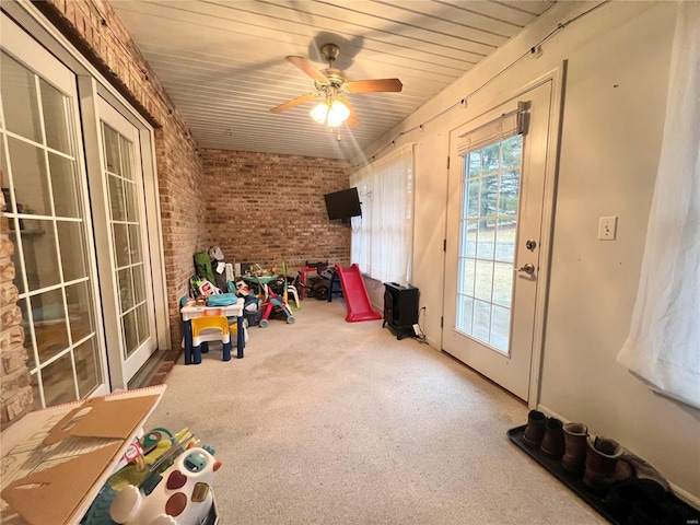 interior space with ceiling fan, brick wall, and carpet floors