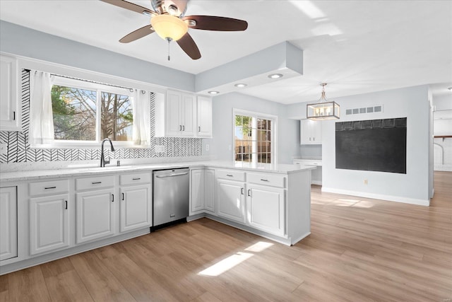 kitchen featuring visible vents, a sink, stainless steel dishwasher, a peninsula, and light wood finished floors