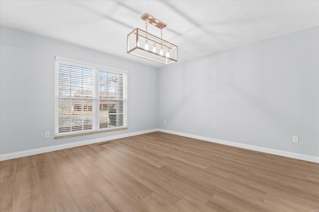 unfurnished dining area with an inviting chandelier, baseboards, and light wood-style floors