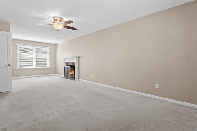 unfurnished living room featuring a ceiling fan, a fireplace, baseboards, and light carpet