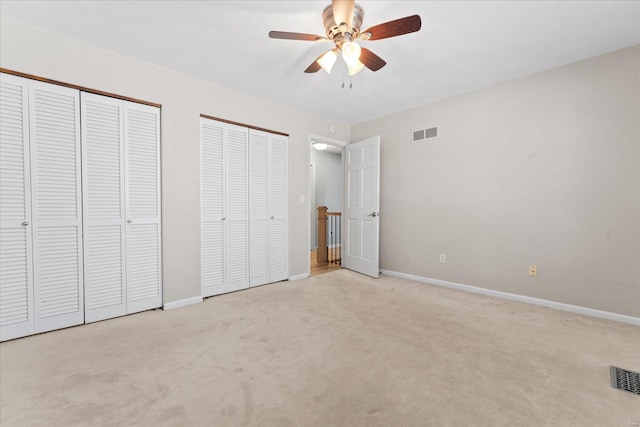 unfurnished bedroom with visible vents, baseboards, two closets, and carpet