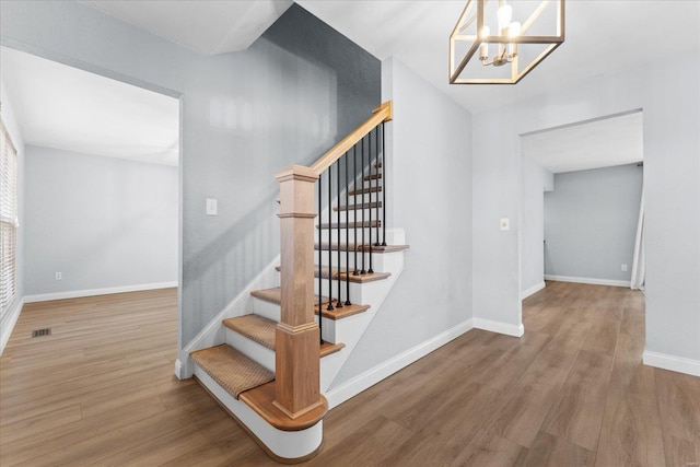 staircase with a chandelier, visible vents, baseboards, and wood finished floors